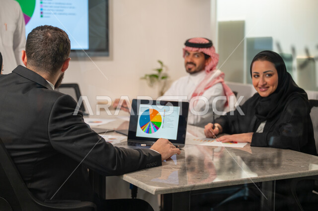  إدارة و تقسيم المهام، فريق عمل عربي خليجي سعودي يقوم بإجراء اجتماع عمل داخل غرفة الاجتماعات في مقر الشركة، شرح و تحليل الرسوم البيانية, دمج الأجهزة التقنية الحديثة بالأعمال المكتبية، دراسة أوراق البيانات الإحصائية, تطوير المشاريع و الاستثمارات