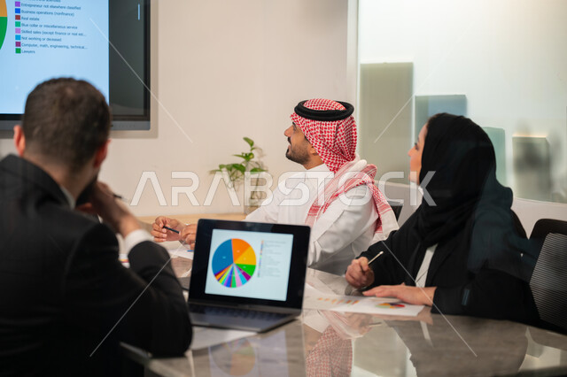  إدارة و تقسيم المهام، فريق عمل عربي خليجي سعودي يقوم بإجراء اجتماع عمل داخل غرفة الاجتماعات في مقر الشركة، شرح و تحليل الرسوم البيانية, دمج الأجهزة التقنية الحديثة بالأعمال المكتبية، دراسة أوراق البيانات الإحصائية, تطوير المشاريع و الاستثمارات