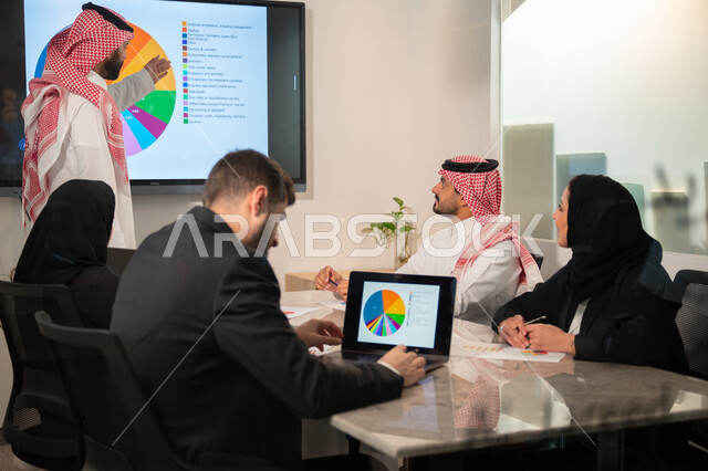  إدارة و تقسيم المهام، فريق عمل عربي خليجي سعودي يقوم بإجراء اجتماع عمل داخل غرفة الاجتماعات في مقر الشركة، شرح و تحليل الرسوم البيانية, دمج الأجهزة التقنية الحديثة بالأعمال المكتبية، دراسة أوراق البيانات الإحصائية, تطوير المشاريع و الاستثمارات