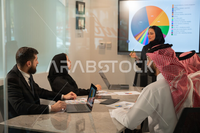  إدارة و تقسيم المهام، فريق عمل عربي خليجي سعودي يقوم بإجراء اجتماع عمل داخل غرفة الاجتماعات في مقر الشركة، شرح و تحليل الرسوم البيانية, دمج الأجهزة التقنية الحديثة بالأعمال المكتبية، دراسة أوراق البيانات الإحصائية, تطوير المشاريع و الاستثمارات