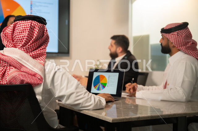  إدارة و تقسيم المهام، فريق عمل عربي خليجي سعودي يقوم بإجراء اجتماع عمل داخل غرفة الاجتماعات في مقر الشركة، شرح و تحليل الرسوم البيانية, دمج الأجهزة التقنية الحديثة بالأعمال المكتبية، دراسة أوراق البيانات الإحصائية, تطوير المشاريع و الاستثمارات