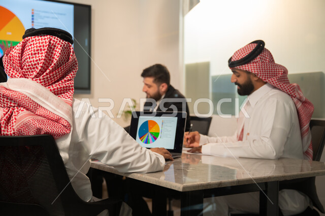  إدارة و تقسيم المهام، فريق عمل عربي خليجي سعودي يقوم بإجراء اجتماع عمل داخل غرفة الاجتماعات في مقر الشركة، شرح و تحليل الرسوم البيانية, دمج الأجهزة التقنية الحديثة بالأعمال المكتبية، دراسة أوراق البيانات الإحصائية, تطوير المشاريع و الاستثمارات