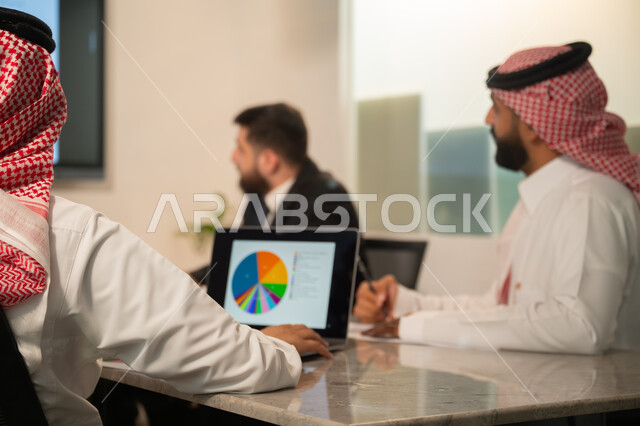  إدارة و تقسيم المهام، فريق عمل عربي خليجي سعودي يقوم بإجراء اجتماع عمل داخل غرفة الاجتماعات في مقر الشركة، شرح و تحليل الرسوم البيانية, دمج الأجهزة التقنية الحديثة بالأعمال المكتبية، دراسة أوراق البيانات الإحصائية, تطوير المشاريع و الاستثمارات