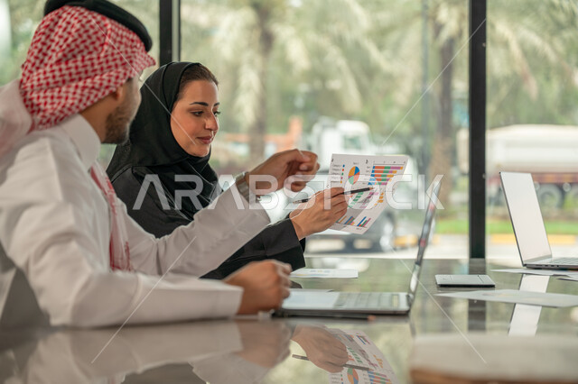  تبادل الخبرات والمعلومات لتحقيق الاهداف, موظفان عربيان خليجيان سعوديان يجلسان على مكتبهم داخل مقر الشركة، استخدام الحاسب والتقنية في مجال الاعمال، بيئة العمل المريحة في الشركات السعودية، الحوار و النقاش بين الزملاء