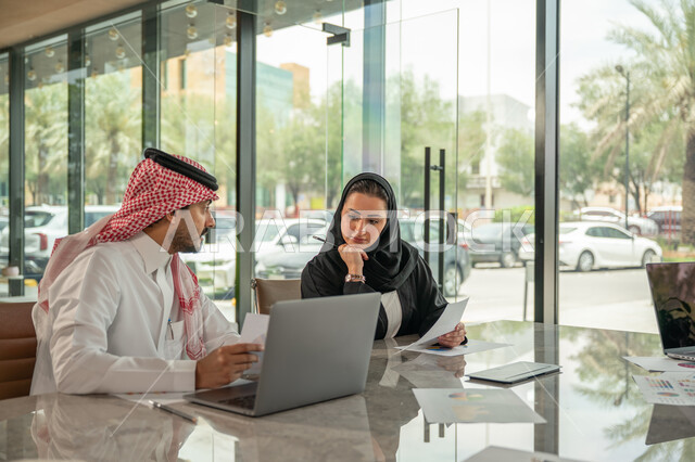  تبادل الخبرات والمعلومات لتحقيق الاهداف, موظفان عربيان خليجيان سعوديان يجلسان على مكتبهم داخل مقر الشركة، استخدام الحاسب والتقنية في مجال الاعمال، بيئة العمل المريحة في الشركات السعودية، الحوار و النقاش بين الزملاء