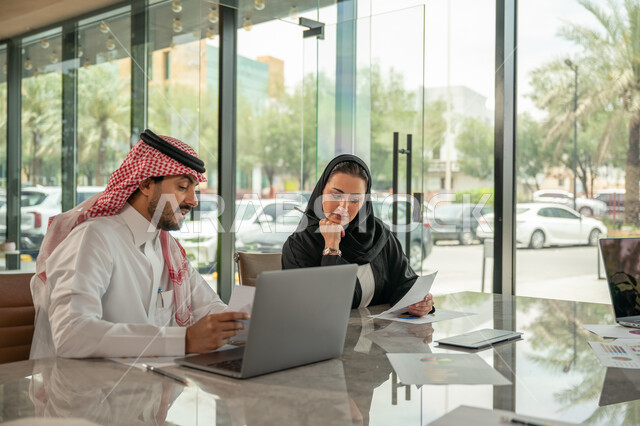  تبادل الخبرات والمعلومات لتحقيق الاهداف, موظفان عربيان خليجيان سعوديان يجلسان على مكتبهم داخل مقر الشركة، استخدام الحاسب والتقنية في مجال الاعمال، بيئة العمل المريحة في الشركات السعودية، الحوار و النقاش بين الزملاء