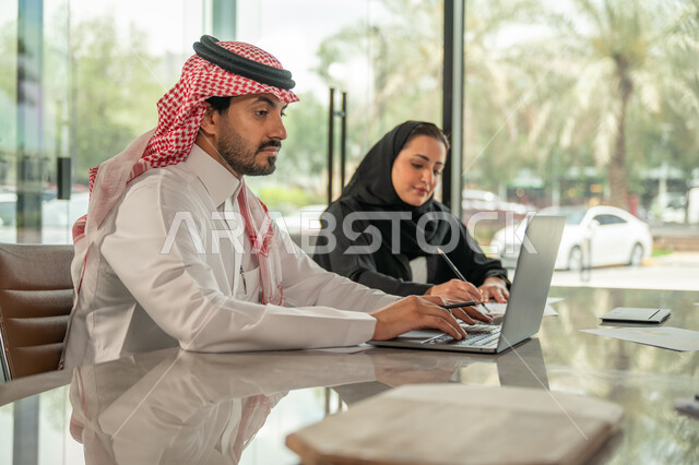  تبادل الخبرات والمعلومات لتحقيق الاهداف, موظفان عربيان خليجيان سعوديان يجلسان على مكتبهم داخل مقر الشركة، استخدام الحاسب والتقنية في مجال الاعمال، بيئة العمل المريحة في الشركات السعودية، الحوار و النقاش بين الزملاء