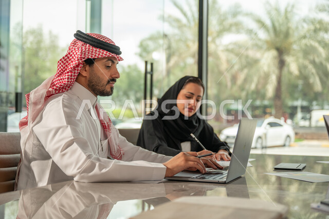  تبادل الخبرات والمعلومات لتحقيق الاهداف, موظفان عربيان خليجيان سعوديان يجلسان على مكتبهم داخل مقر الشركة، استخدام الحاسب والتقنية في مجال الاعمال، بيئة العمل المريحة في الشركات السعودية، الحوار و النقاش بين الزملاء