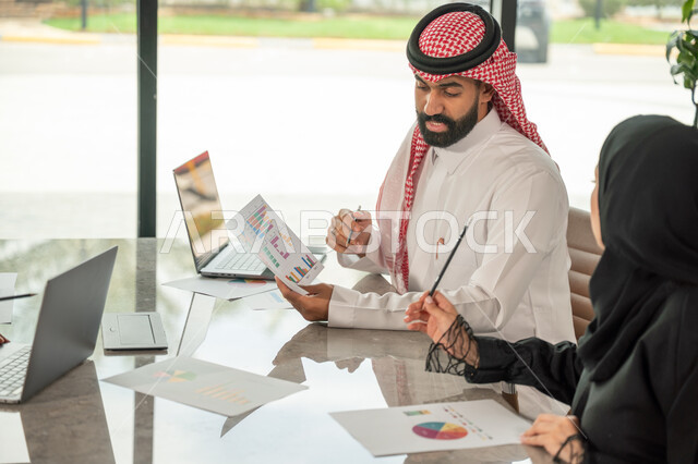  تبادل الخبرات والمعلومات لتحقيق الاهداف, موظفان عربيان خليجيان سعوديان يجلسان على مكتبهم داخل مقر الشركة، استخدام الحاسب والتقنية في مجال الاعمال، بيئة العمل المريحة في الشركات السعودية، الحوار و النقاش بين الزملاء