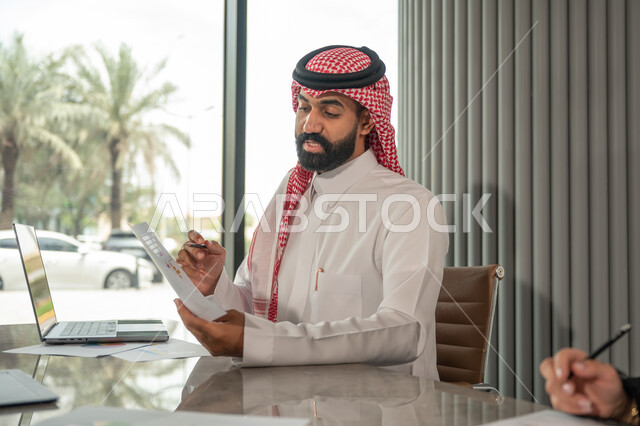  تبادل الخبرات والمعلومات لتحقيق الاهداف, موظفان عربيان خليجيان سعوديان يجلسان على مكتبهم داخل مقر الشركة، استخدام الحاسب والتقنية في مجال الاعمال، بيئة العمل المريحة في الشركات السعودية، الحوار و النقاش بين الزملاء