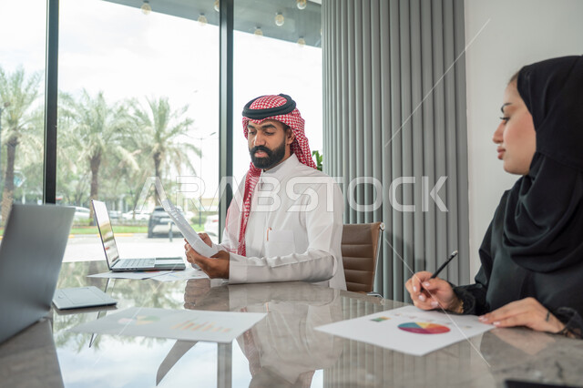  تبادل الخبرات والمعلومات لتحقيق الاهداف, موظفان عربيان خليجيان سعوديان يجلسان على مكتبهم داخل مقر الشركة، استخدام الحاسب والتقنية في مجال الاعمال، بيئة العمل المريحة في الشركات السعودية، الحوار و النقاش بين الزملاء