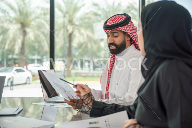  تبادل الخبرات والمعلومات لتحقيق الاهداف, موظفان عربيان خليجيان سعوديان يجلسان على مكتبهم داخل مقر الشركة، استخدام الحاسب والتقنية في مجال الاعمال، بيئة العمل المريحة في الشركات السعودية، الحوار و النقاش بين الزملاء