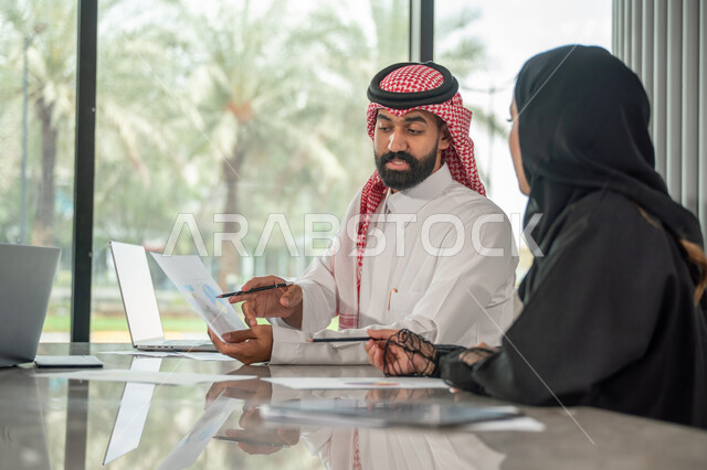  تبادل الخبرات والمعلومات لتحقيق الاهداف, موظفان عربيان خليجيان سعوديان يجلسان على مكتبهم داخل مقر الشركة، استخدام الحاسب والتقنية في مجال الاعمال، بيئة العمل المريحة في الشركات السعودية، الحوار و النقاش بين الزملاء