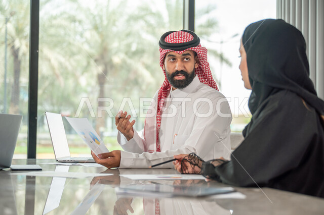  تبادل الخبرات والمعلومات لتحقيق الاهداف, موظفان عربيان خليجيان سعوديان يجلسان على مكتبهم داخل مقر الشركة، استخدام الحاسب والتقنية في مجال الاعمال، بيئة العمل المريحة في الشركات السعودية، الحوار و النقاش بين الزملاء