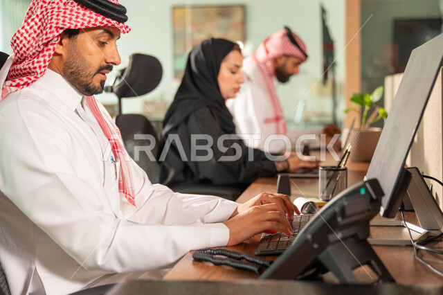  تبادل الخبرات والمعلومات لتحقيق الاهداف, موظفان عربيان خليجيان سعوديان يجلسان على مكتبهم داخل مقر الشركة، استخدام الحاسب والتقنية في مجال الاعمال، بيئة العمل المريحة في الشركات السعودية، الحوار و النقاش بين الزملاء