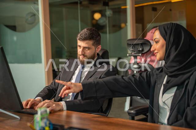 تبادل الخبرات والمعلومات لتحقيق الاهداف, موظفان عربيان خليجيان سعوديان يجلسان على مكتبهم داخل مقر الشركة، استخدام الحاسب والتقنية في مجال الاعمال، بيئة العمل المريحة في الشركات السعودية، الحوار و النقاش بين الزملاء