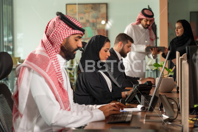  تبادل الخبرات والمعلومات لتحقيق الاهداف, موظفان عربيان خليجيان سعوديان يجلسان على مكتبهم داخل مقر الشركة، استخدام الحاسب والتقنية في مجال الاعمال، بيئة العمل المريحة في الشركات السعودية، الحوار و النقاش بين الزملاء