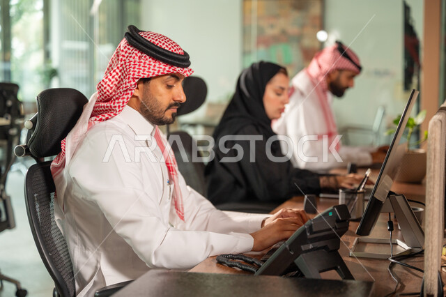  استخدام الحاسب والتقنية في مجال الاعمال، بيئة العمل المريحة في الشركات السعودية، الحوار و النقاش بين الزملاء، تبادل الخبرات والمعلومات لتحقيق الاهداف, موظفان عربيان خليجيان سعوديان يجلسان على مكتبهم داخل مقر الشركة