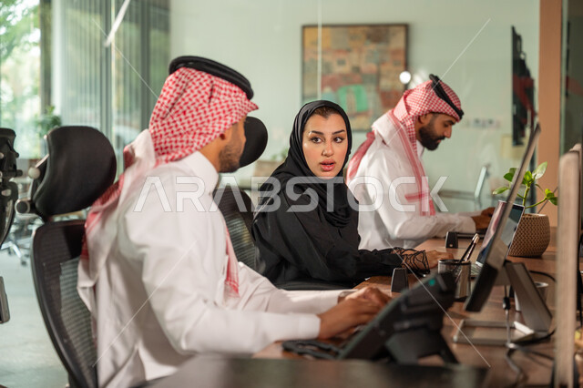  استخدام الحاسب والتقنية في مجال الاعمال، بيئة العمل المريحة في الشركات السعودية، الحوار و النقاش بين الزملاء، تبادل الخبرات والمعلومات لتحقيق الاهداف, موظفان عربيان خليجيان سعوديان يجلسان على مكتبهم داخل مقر الشركة
