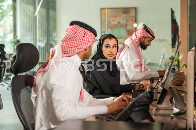 استخدام الحاسب والتقنية في مجال الاعمال، بيئة العمل المريحة في الشركات السعودية، الحوار و النقاش بين الزملاء، تبادل الخبرات والمعلومات لتحقيق الاهداف, موظفان عربيان خليجيان سعوديان يجلسان على مكتبهم داخل مقر الشركة
