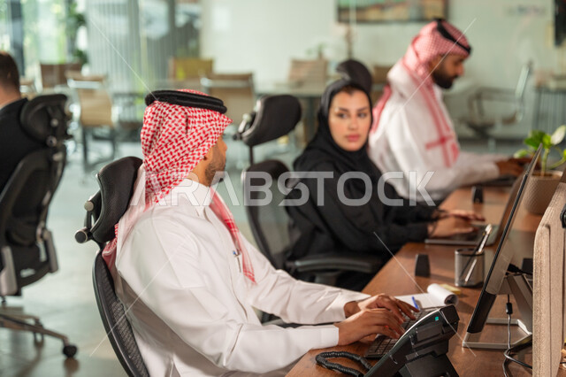  استخدام الحاسب والتقنية في مجال الاعمال، بيئة العمل المريحة في الشركات السعودية، الحوار و النقاش بين الزملاء، تبادل الخبرات والمعلومات لتحقيق الاهداف, موظفان عربيان خليجيان سعوديان يجلسان على مكتبهم داخل مقر الشركة