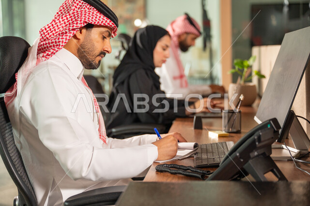  استخدام الحاسب والتقنية في مجال الاعمال، بيئة العمل المريحة في الشركات السعودية، الحوار و النقاش بين الزملاء، تبادل الخبرات والمعلومات لتحقيق الاهداف, موظفان عربيان خليجيان سعوديان يجلسان على مكتبهم داخل مقر الشركة