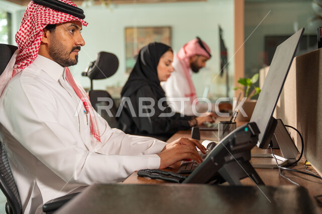  استخدام الحاسب والتقنية في مجال الاعمال، بيئة العمل المريحة في الشركات السعودية، الحوار و النقاش بين الزملاء، تبادل الخبرات والمعلومات لتحقيق الاهداف, موظفان عربيان خليجيان سعوديان يجلسان على مكتبهم داخل مقر الشركة