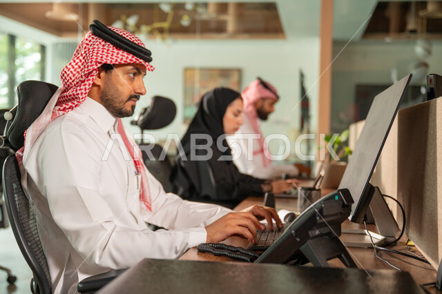  استخدام الحاسب والتقنية في مجال الاعمال، بيئة العمل المريحة في الشركات السعودية، الحوار و النقاش بين الزملاء، تبادل الخبرات والمعلومات لتحقيق الاهداف, موظفان عربيان خليجيان سعوديان يجلسان على مكتبهم داخل مقر الشركة