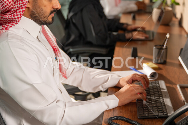  استخدام الحاسب والتقنية في مجال الاعمال، بيئة العمل المريحة في الشركات السعودية، الحوار و النقاش بين الزملاء، تبادل الخبرات والمعلومات لتحقيق الاهداف, موظفان عربيان خليجيان سعوديان يجلسان على مكتبهم داخل مقر الشركة
