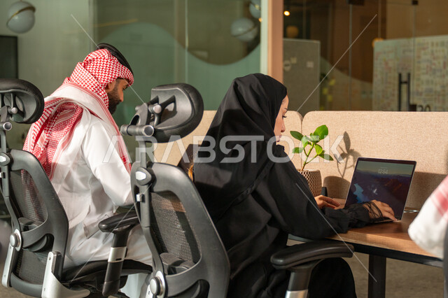  استخدام الحاسب والتقنية في مجال الاعمال، بيئة العمل المريحة في الشركات السعودية، الحوار و النقاش بين الزملاء، تبادل الخبرات والمعلومات لتحقيق الاهداف, موظفان عربيان خليجيان سعوديان يجلسان على مكتبهم داخل مقر الشركة