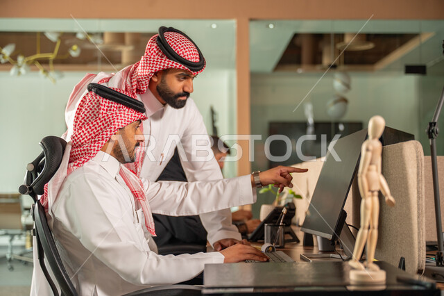  استخدام الحاسب والتقنية في مجال الاعمال، بيئة العمل المريحة في الشركات السعودية، الحوار و النقاش بين الزملاء، تبادل الخبرات والمعلومات لتحقيق الاهداف, موظفان عربيان خليجيان سعوديان يجلسان على مكتبهم داخل مقر الشركة