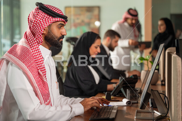  استخدام الحاسب والتقنية في مجال الاعمال، بيئة العمل المريحة في الشركات السعودية، الحوار و النقاش بين الزملاء، تبادل الخبرات والمعلومات لتحقيق الاهداف, موظفان عربيان خليجيان سعوديان يجلسان على مكتبهم داخل مقر الشركة