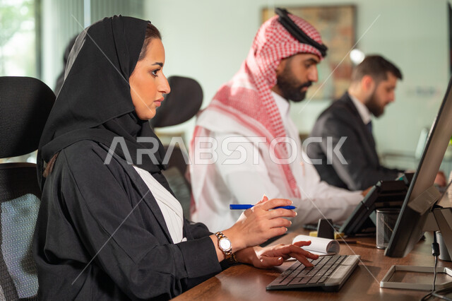  استخدام الحاسب والتقنية في مجال الاعمال، بيئة العمل المريحة في الشركات السعودية، الحوار و النقاش بين الزملاء، تبادل الخبرات والمعلومات لتحقيق الاهداف, موظفان عربيان خليجيان سعوديان يجلسان على مكتبهم داخل مقر الشركة