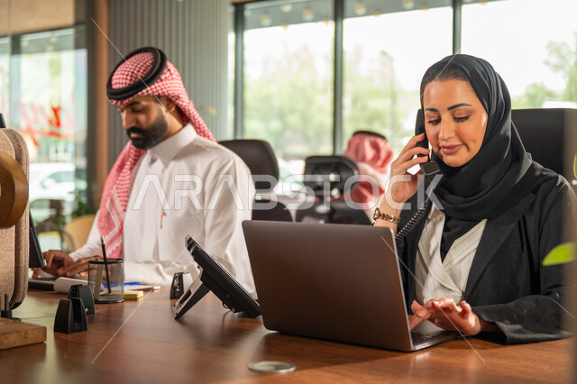 مفهوم الاستعلامات والاستفسارات، موظفة عربية خليجية سعودية محجبة مبتسمة تعمل في خدمة العملاء تقوم بالرد على الهاتف، الاجابه والرد على الأسئلة، العمل وادخال البيانات على الحاسوب، متابعة وتطوير العمل