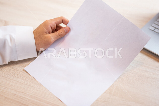 رجل عربي خليجي سعودي يجلس امام الحاسوب المحمول، أوراق بيضاء فارغة، سكرتير يدير الأعمال الورقية، اعمال مكتبية