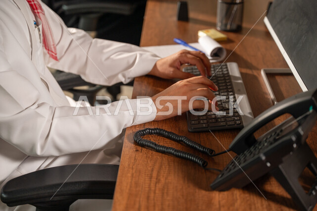 Gestures and expressions of concentration, Saudi office jobs and professions, writing and recording data and results, managing and completing tasks using a modern and advanced technical device, a close-up side view of a Saudi Arabian Gulf man wearing a traditional shemagh and thobe working on a laptop