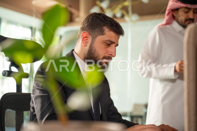 ادارة وانجاز المهام باستخدام جهاز تقني حديث ومتطور, صورة مقربة من الجانب لرجل عربي خليجي سعودي يرتدي البدلة الرسمية يعمل على الحاسوب المحمول، ايماءات وتعابير التركيز، مهن ووظائف مكتبية سعودية، كتابة وتدوين البيانات والنتائج