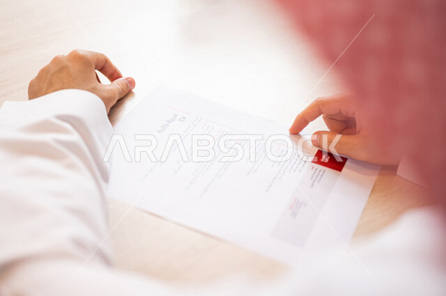 رجل عربي خليجي سعودي يقوم بقراءة اوراق خاصة بالسيرة الذاتية، سكرتير يدير الاعمال الورقية، قراءة السيرة الذاتية، مفهوم التوظيف والعمل، أعمال مكتبية