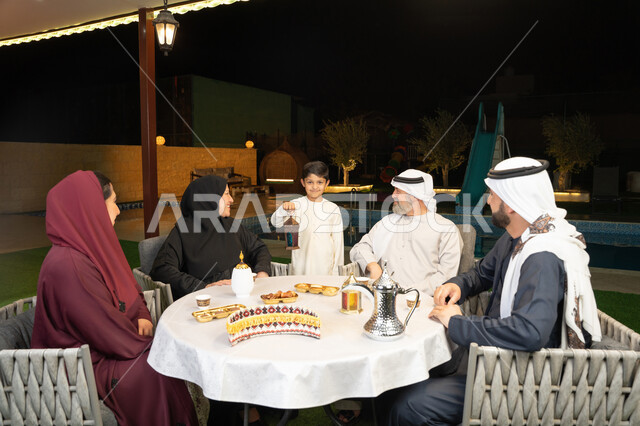 زينة وديكور المناسبات والأعياد الاسلامية، اجتماع العائلة في شهر رمضان المبارك، ملاطفة الأجداد للحفيد، أسرة عربية خليجية إماراتية تقضي وقت ممتع في جلسة خارجية في احدى الشاليهات، ولد يحمل بيده فانوس معدني مضيء