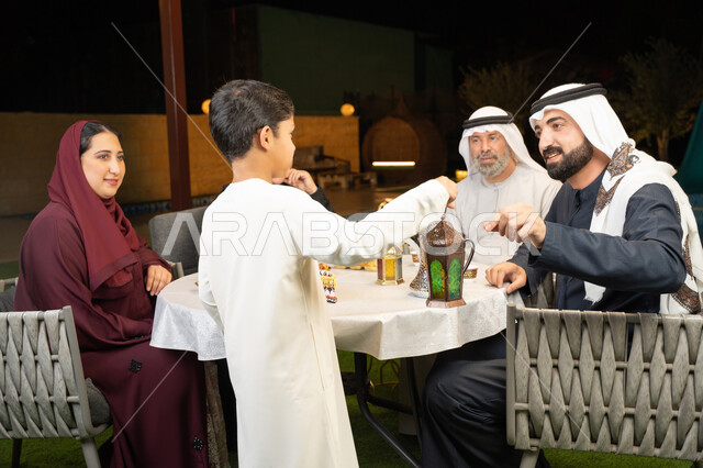 قضاء وقت ممتع في جلسة خارجية في احدى الشاليهات، ديكور وزينة المناسبات والأعياد الاسلامية، اجتماع العائلة في شهر رمضان المبارك، صورة من الخلف لولد عربي خليجي اماراتي يحمل بيده فانوس معدني مضيء