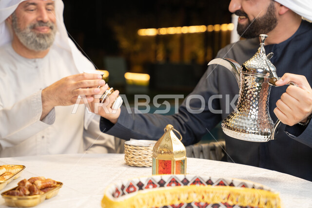 أصالة العادات والتقاليد الأصيلة, التمسك بالقيم الكريمة المتوارثة من الأجداد، الاستمتاع بالمشروبات الساخنة, منتج محلي وطني، كرم الضيافة وحسن الاستقبال, صورة مقربة ليد رجل عربي خليجي اماراتي يقوم بصب القهوة من الدلة الفضية، زينة وديكور شهر رمضان المبارك