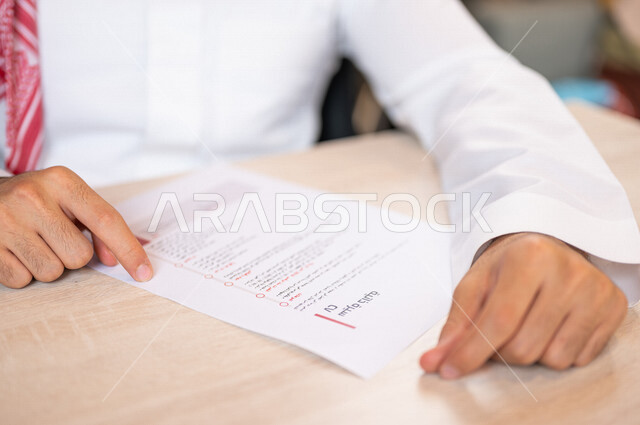 رجل عربي خليجي سعودي يقوم بقراءة اوراق خاصة بالسيرة الذاتية، سكرتير يدير الاعمال الورقية، قراءة السيرة الذاتية، مفهوم التوظيف والعمل، أعمال مكتبية