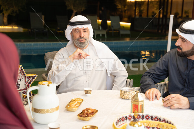 أجواء ليلية رمضانية روحانية، زينة المناسبات الإسلامية، مفهوم الترابط الأسري، كرم الضيافة وحسن الاستقبال في شهر رمضان المبارك، تبادل الأحاديث بين أفراد الأسرة، عائلة عربية خليجية اماراتية مجتمعة في جلسة خارجية في احدى الشاليهات