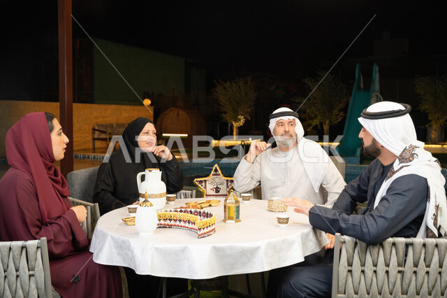 زينة المناسبات الإسلامية، مفهوم الترابط الأسري، كرم الضيافة وحسن الاستقبال في شهر رمضان المبارك، تبادل الأحاديث بين أفراد الأسرة، أجواء عائلية دينية رمضانية سعيدة، عائلة عربية خليجية اماراتية مجتمعة في جلسة ليلية خارجية في احدى الشاليهات