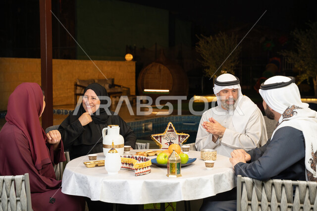 زينة المناسبات الإسلامية، مفهوم الترابط الأسري، كرم الضيافة وحسن الاستقبال في شهر رمضان المبارك، تبادل الأحاديث بين أفراد الأسرة، أجواء عائلية دينية رمضانية سعيدة، عائلة عربية خليجية اماراتية مجتمعة في جلسة ليلية خارجية في احدى الشاليهات