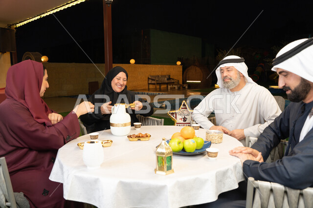 حسن الضيافة والاستقبال، التسامر وتبادل الأحاديث بين أفراد الأسرة، تعابير السعادة والسرور بلمة الأهل، ديكور وزينة شهر رمضان المبارك، جلسة عائلية رمضانية روحانية، امرأة عربية خليجية اماراتية تجلس مع عائلتها وتقوم بتقديم التمر