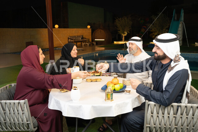 حسن الضيافة والاستقبال، التسامر وتبادل الأحاديث بين أفراد الأسرة، تعابير السعادة والسرور بلمة الأهل، ديكور وزينة شهر رمضان المبارك، جلسة عائلية رمضانية روحانية، امرأة عربية خليجية اماراتية تجلس مع عائلتها وتقوم بتقديم التمر