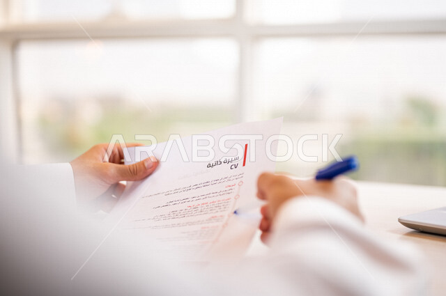 رجل عربي خليجي سعودي يقوم بقراءة اوراق خاصة بالسيرة الذاتية، سكرتير يدير الاعمال الورقية، قراءة السيرة الذاتية، مفهوم التوظيف والعمل، أعمال مكتبية
