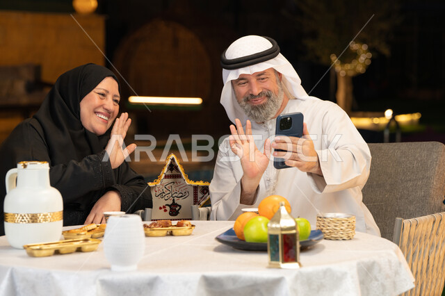 التواصل عبر الوسائل التقنية الحديثة، قضاء وقت ممتع في جلسة خارجية في احدى الشاليهات، زينة وديكور المناسبات والأعياد الاسلامية، أجواء عائلية سعيدة في شهر رمضان المبارك، زوجان عربيان خليجيان اماراتيان يقومان بإجراء مكالمة فيديو بإيماءات السعادة والسرور