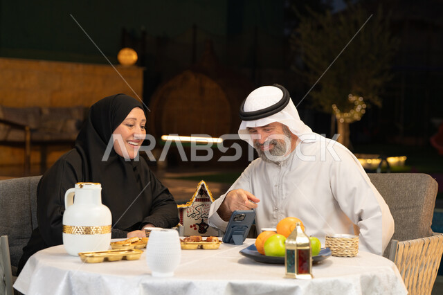 استخدام الوسائل التقنية الحديثة، قضاء وقت ممتع في جلسة خارجية في احدى الشاليهات، زينة وديكور المناسبات والأعياد الاسلامية، أجواء عائلية سعيدة في شهر رمضان المبارك، زوجان عربيان خليجيان اماراتيان يقومان بإجراء مكالمة فيديو بإيماءات السعادة والسرور